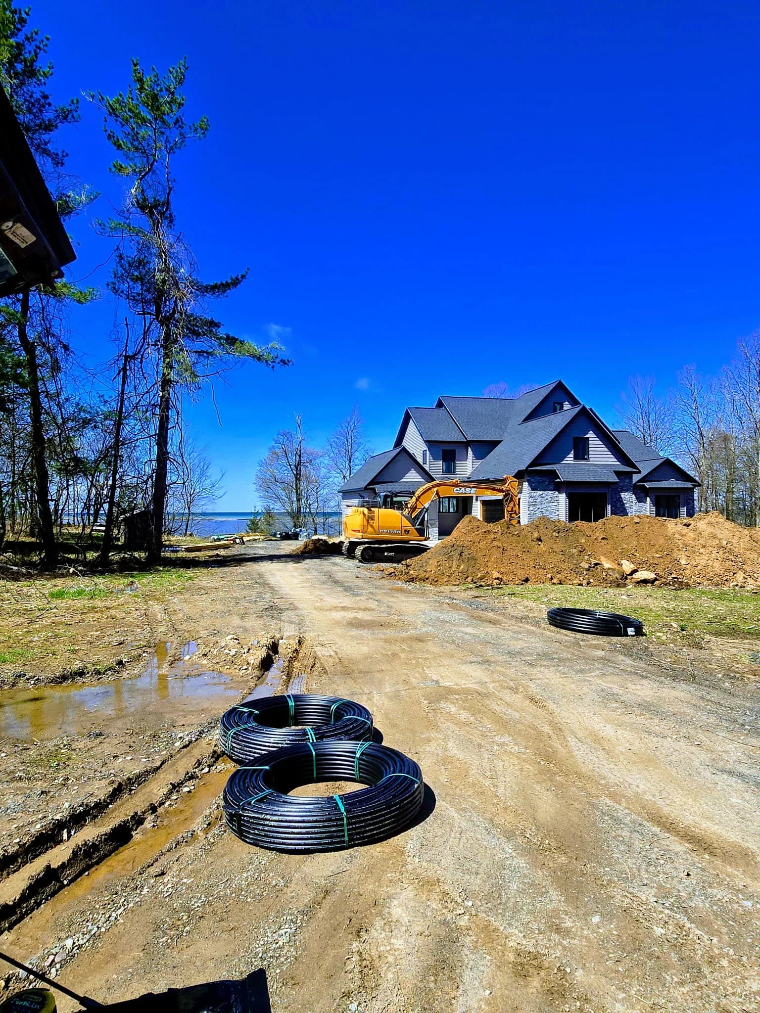 Excavation underway at a large new-construction home — geothermal pipe coils staged for installation in the loop field.