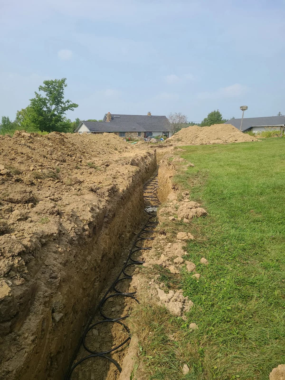 Long trench across a residential lot with geothermal loop piping laid in before backfilling.