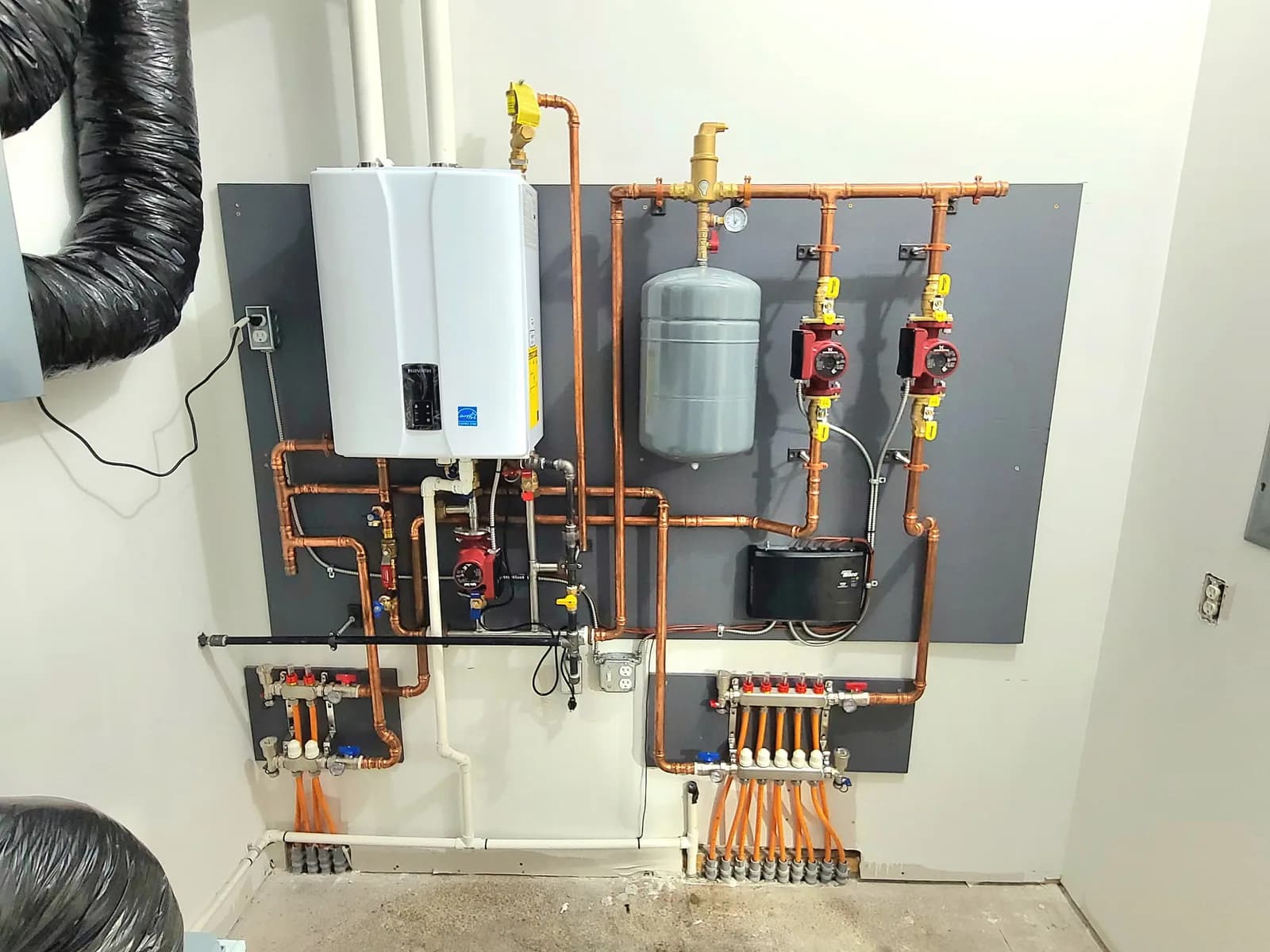 Wall-mounted hydronic heating system with tankless boiler, expansion tank, and radiant floor manifolds — 4th Gen install.