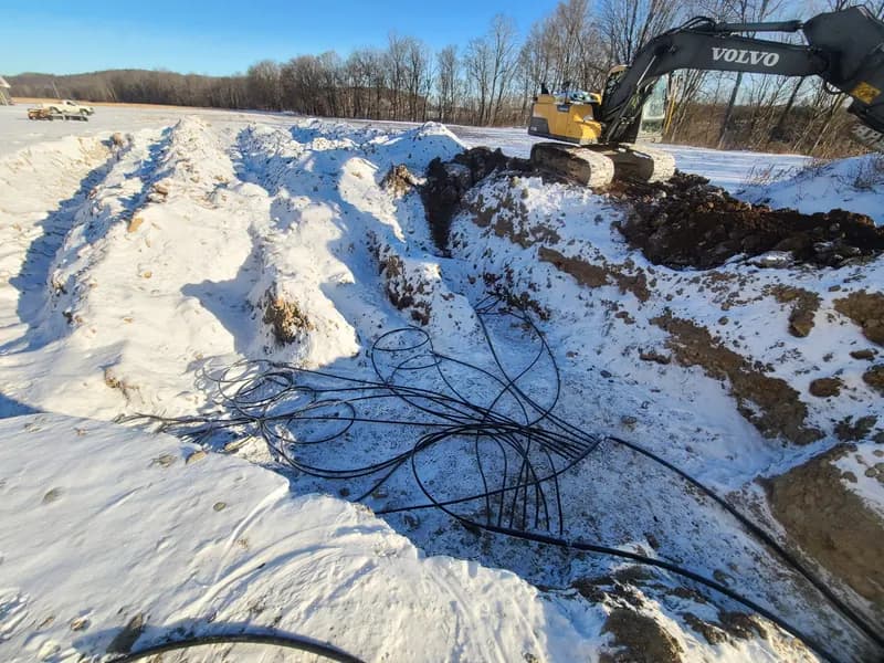 Geothermal ground-loop trench cut through snow at a Monroe County property — winter install.